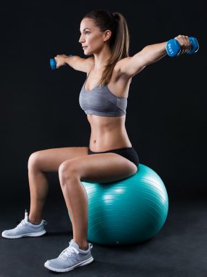 Portrait of beautiful young woman lifting dumbbells over black background.